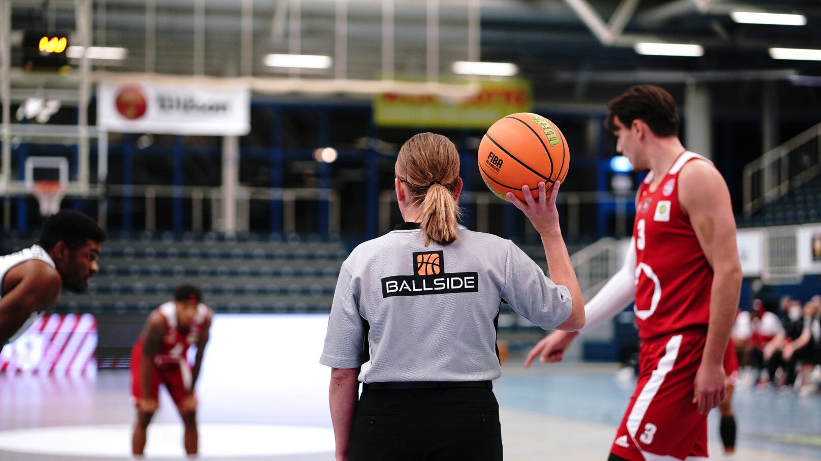 Schiedsrichterin mit Basketball bei der Spielleitung in einer Halle.
